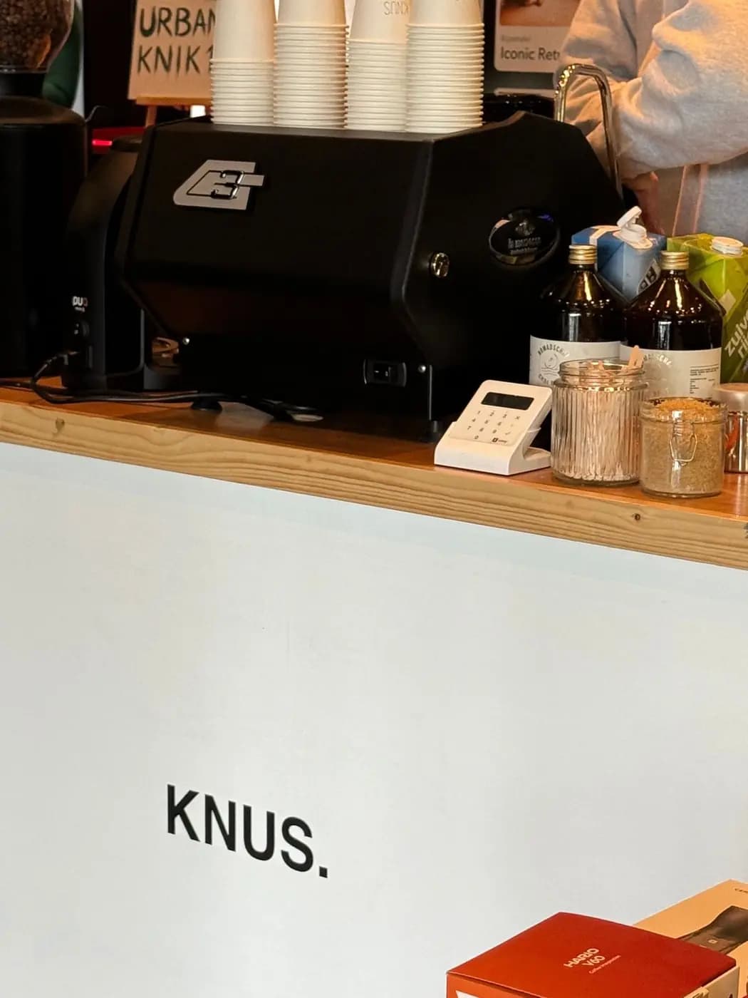 De bar van KNUS met de espressomachine en het KNUS-logo op de toonbank.