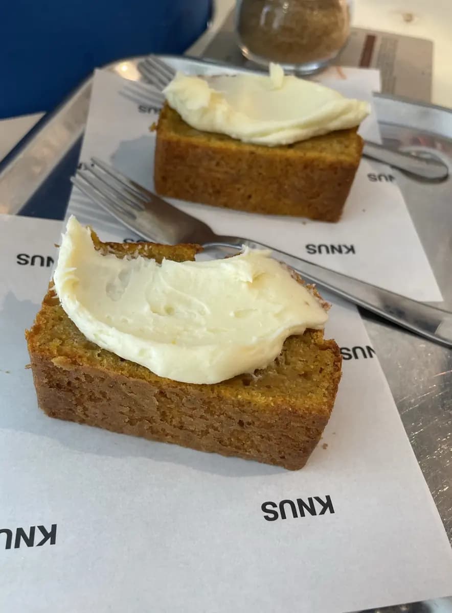 Twee plakken zelfgemaakt gebak met een dikke laag roomkaas, op servetten met het KNUS-logo.