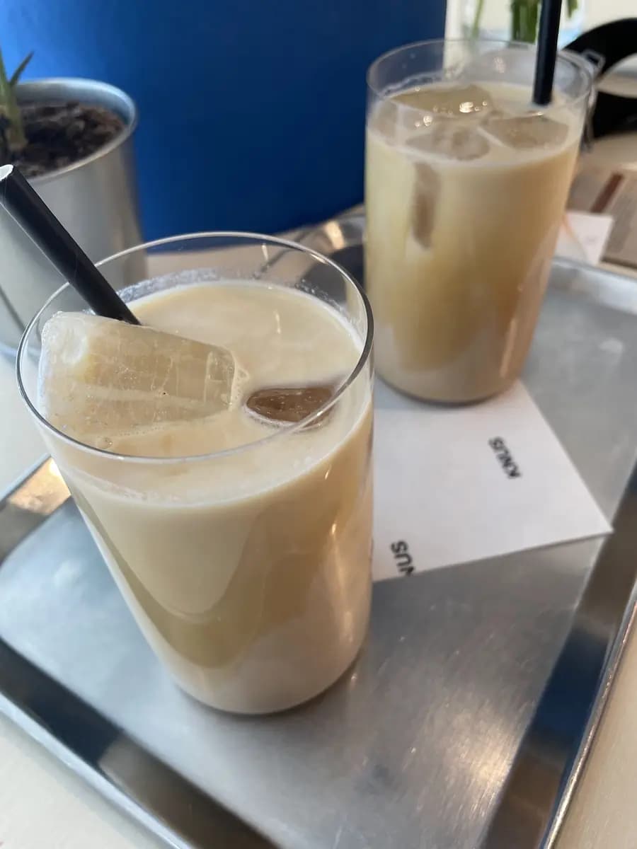 Twee iced lattes op een stalen dienblad voor de kobaltblauwe wand van de bar.